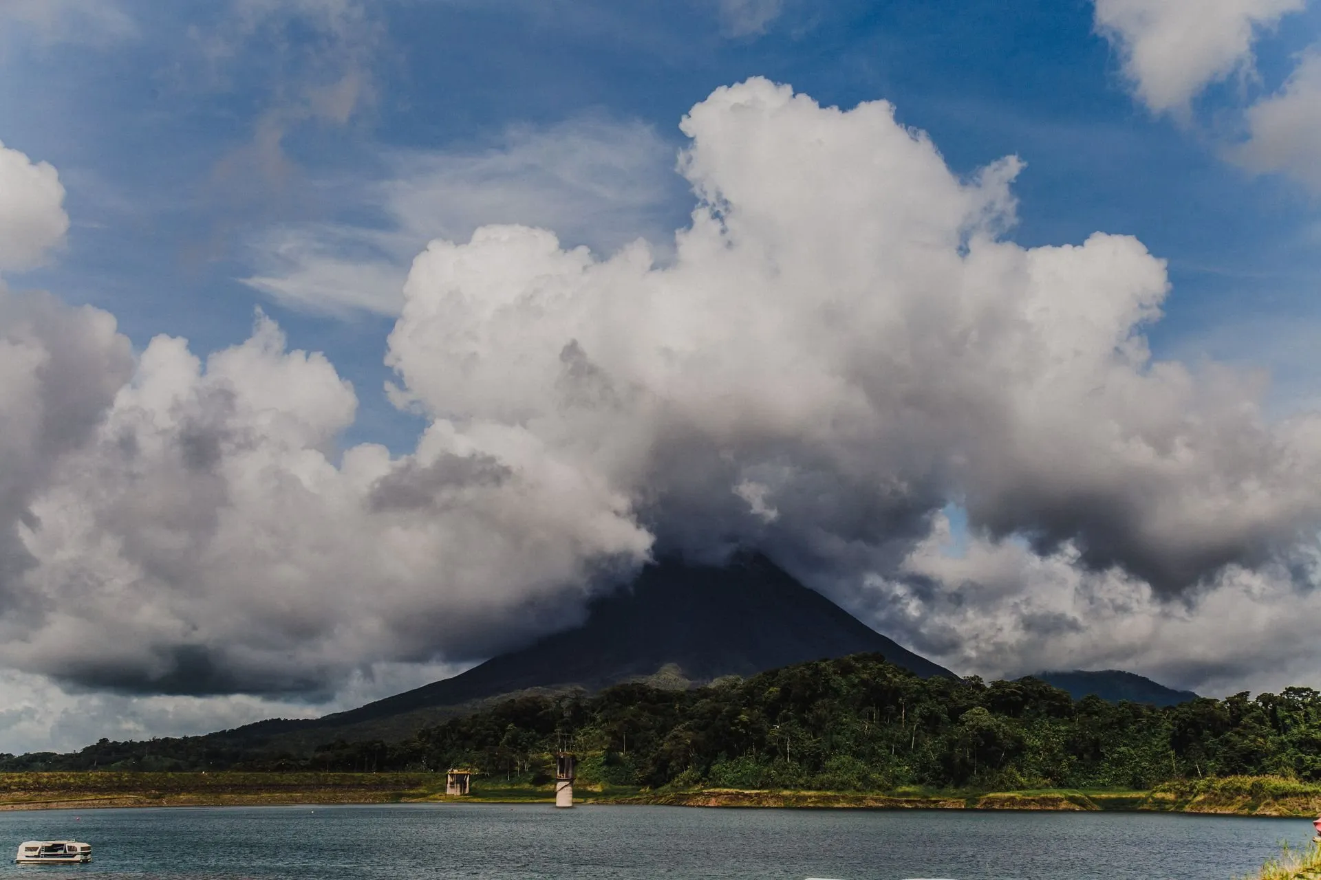 Arenal Volcano under white clouds above a calm lake