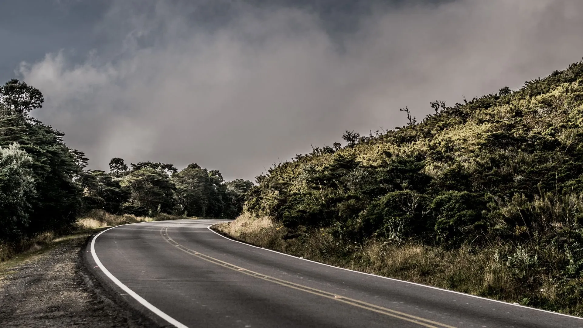 A winding road through green hills in Cartago, Costa Rica, under a cloudy sky